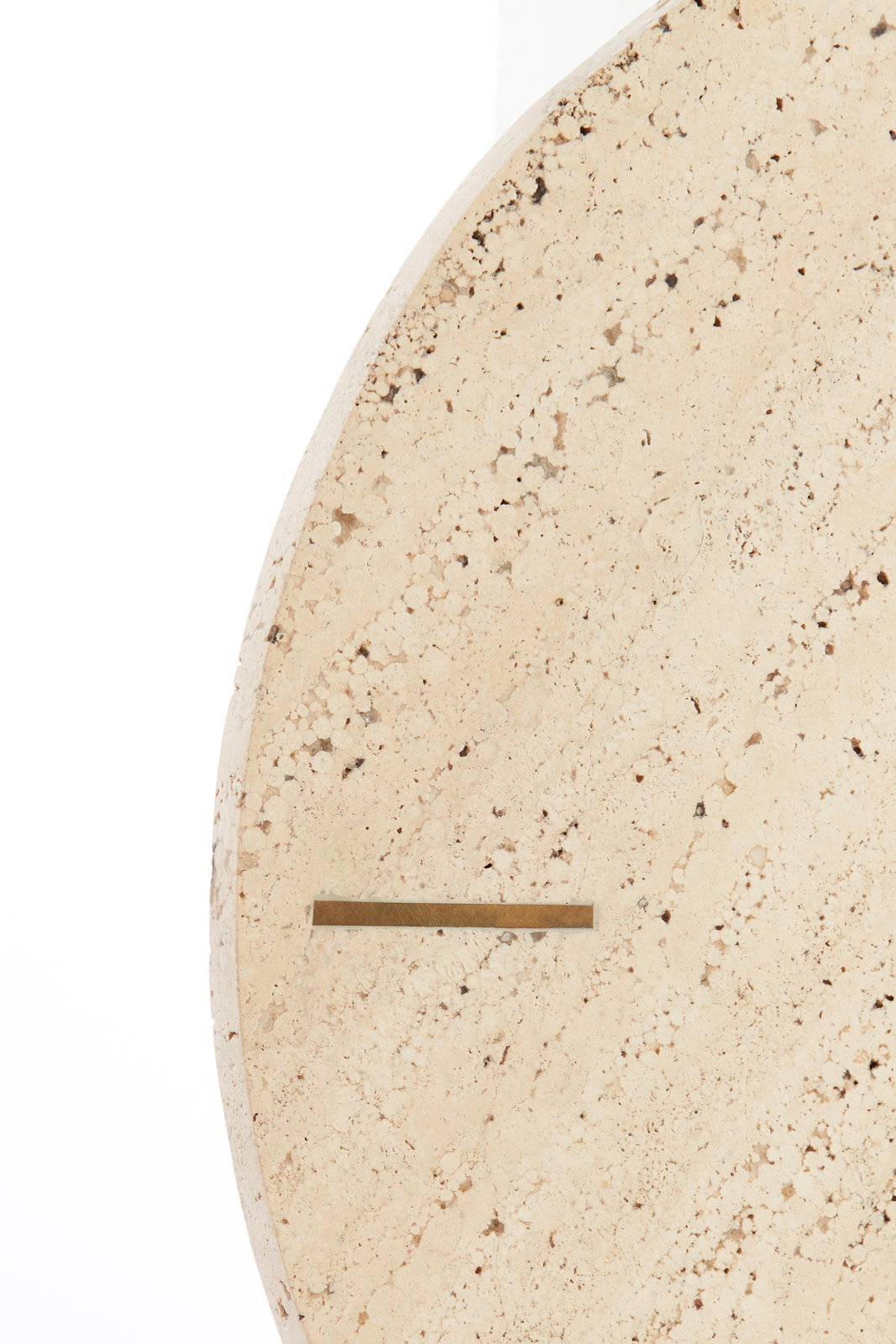 Close-up van een ronde klok van licht, gespikkeld steenmateriaal met een minimalistisch ontwerp, gezien vanaf de zijkant.