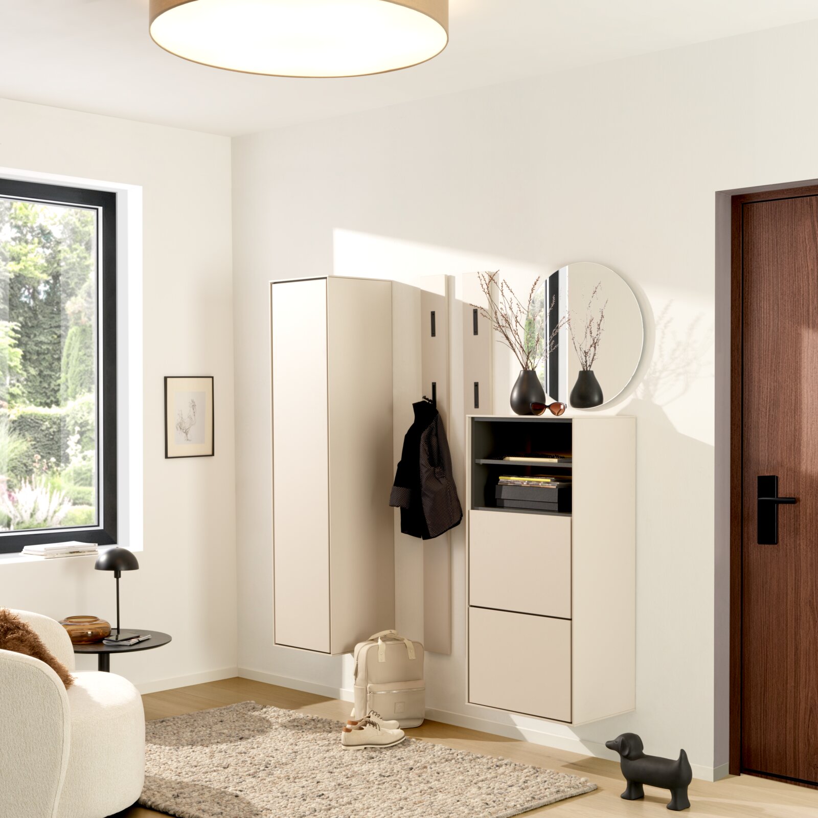 Voleo Hangende schoenenkast RENO Moderne, aan de muur bevestigde garderobeset in wit, bestaande uit een hoge kast, een paneel met haken en een schoenenkast met legplank, evenals een ronde spiegel in de lichte gang; gefotografeerd vanuit een licht zijdelings vooraanzicht