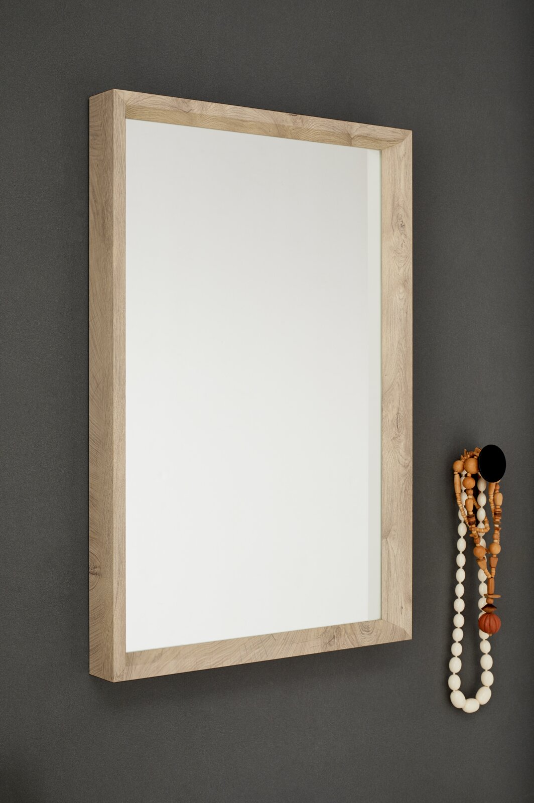 Rechteckiger Wandspiegel mit breitem Holzrahmen in heller Eichenoptik an dunkelgrauer Wand, schräg aus frontaler Perspektive (leicht von links) fotografiert