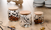 Drei Glasdosen mit Holzdeckeln auf einem Holztisch, dekoriert mit Pfotenabdrücken, Knochen und Fischgräten. Die mittlere Dose zeigt das Wort 'LOVE' mit Pfeilen. Perspektive: Frontalansicht.