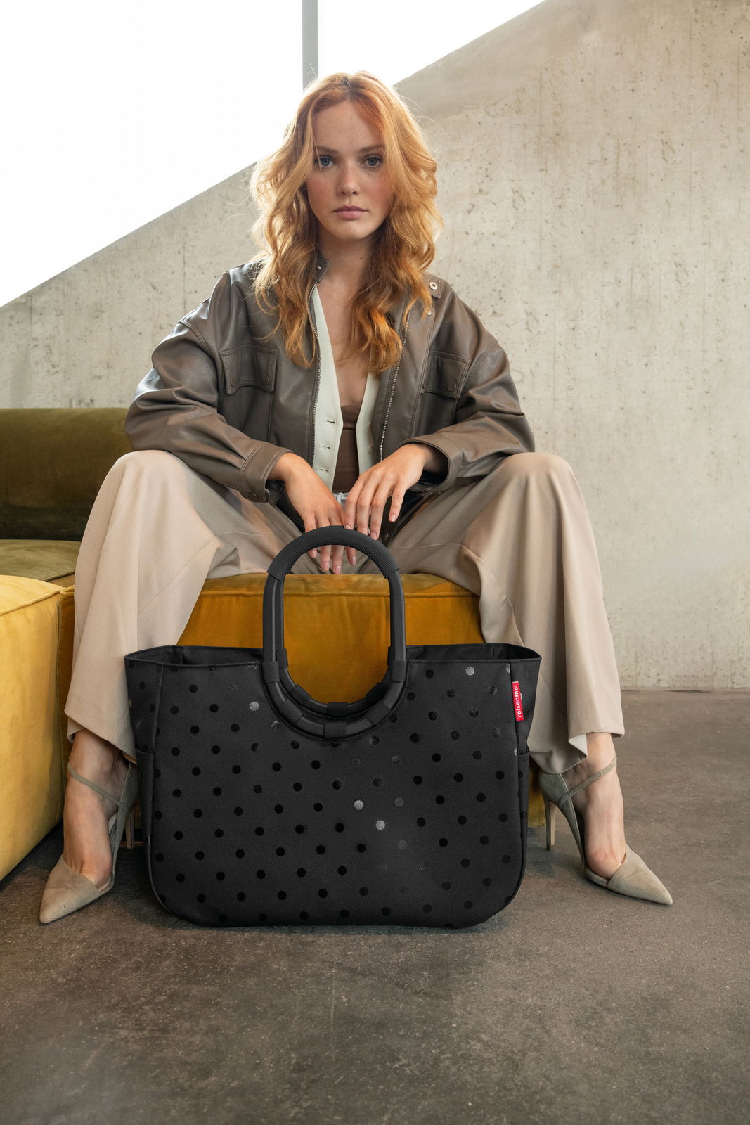 Frau sitzt auf einem Sofa und hält eine schwarze Tasche mit Punkten, Vorderansicht