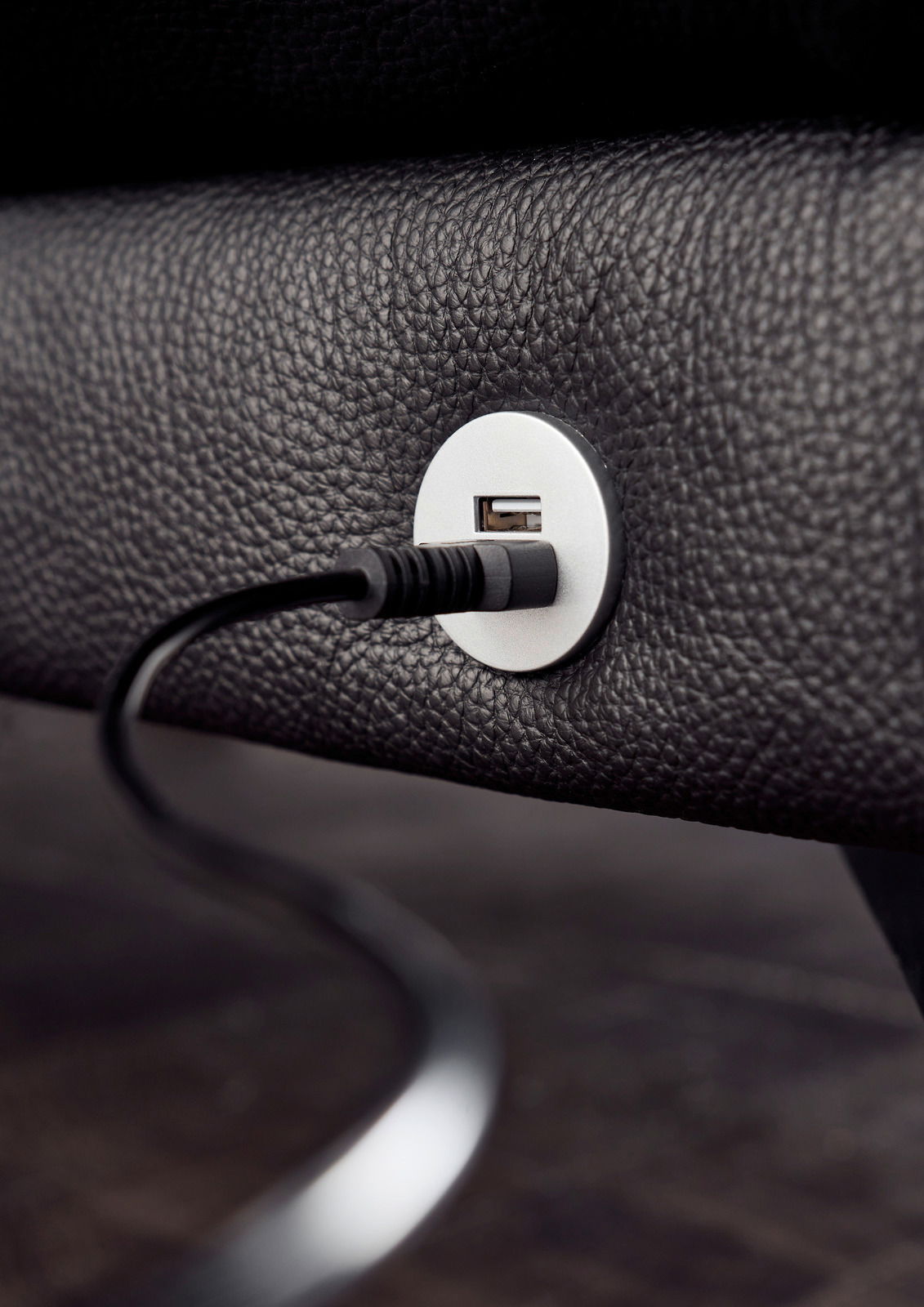 Nahaufnahme eines USB-Anschlusses in einem schwarzen Ledersofa, mit eingestecktem Kabel, seitliche Perspektive.
