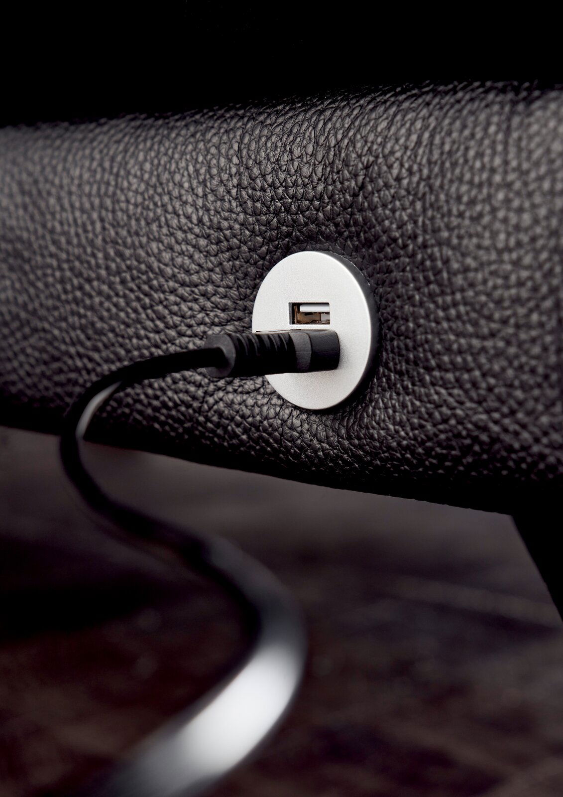Nahaufnahme eines USB-Anschlusses in einem schwarzen Ledersofa, mit eingestecktem Kabel, seitliche Perspektive.