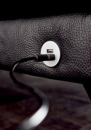 Nahaufnahme eines USB-Anschlusses in einem schwarzen Ledersofa, mit eingestecktem Kabel, seitliche Perspektive.