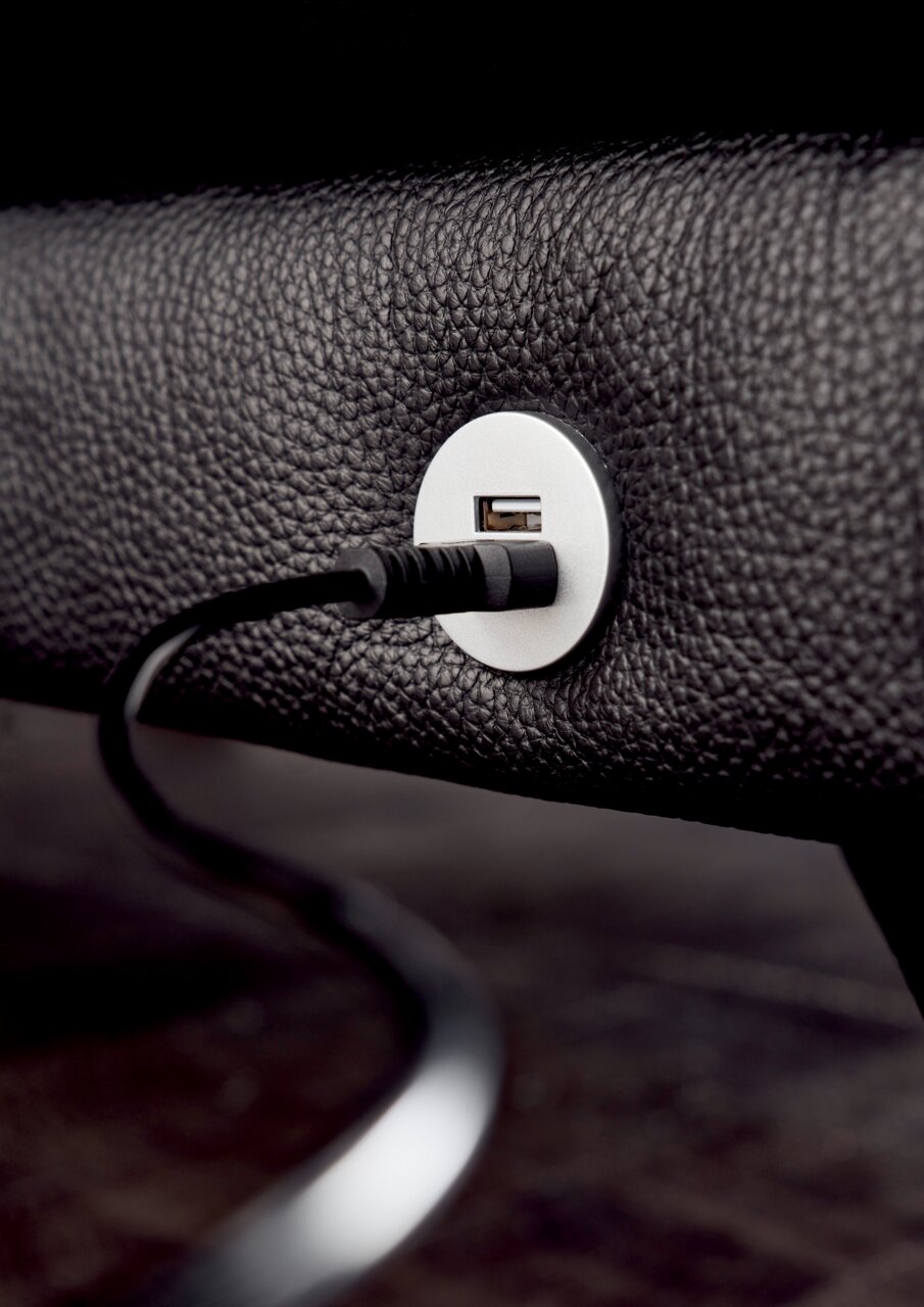 Nahaufnahme eines USB-Anschlusses in einem schwarzen Ledersofa, mit eingestecktem Kabel, seitliche Perspektive.