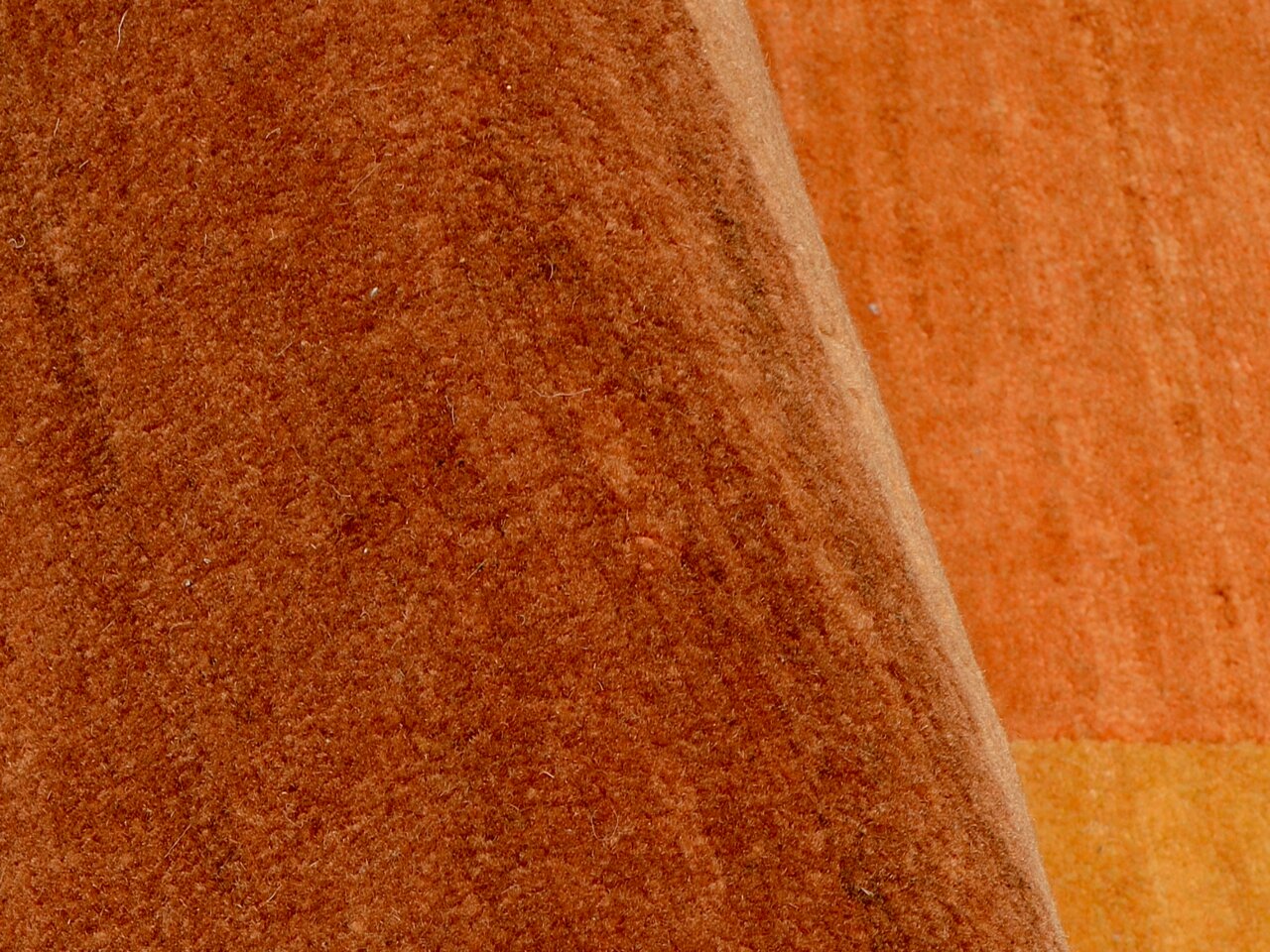 Nahaufnahme eines orangefarbenen Wollteppichs mit sichtbarer Textur und einer Ecke, die leicht umgeschlagen ist.