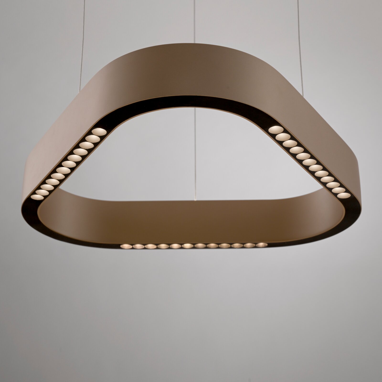 Moderne, dreieckige LED-Pendelleuchte in hellem Beige mit schwarzer Innenkante und integrierten Lichtpunkten, von unten in leichter Untersicht fotografiert