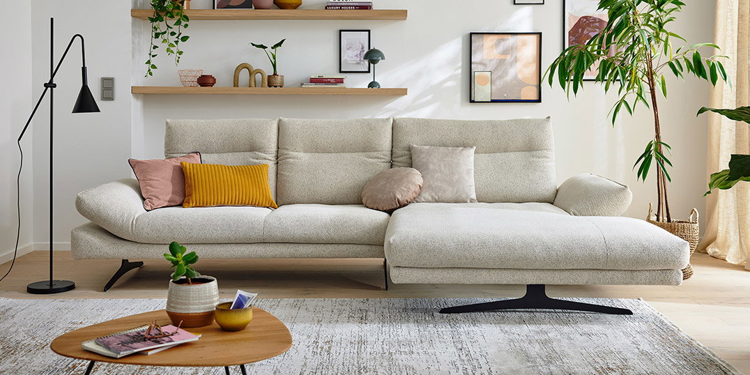 Moderne woonkamer met een lichte hoekbank, kussens, planten en wandplanken in Scandinavische stijl