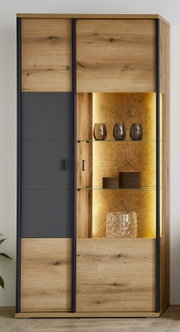 Moderne Vitrine aus hellem Holz mit schwarzer Front und offenem, beleuchtetem Glasregalbereich; frontal aus leichter Schrägansicht von rechts fotografiert.