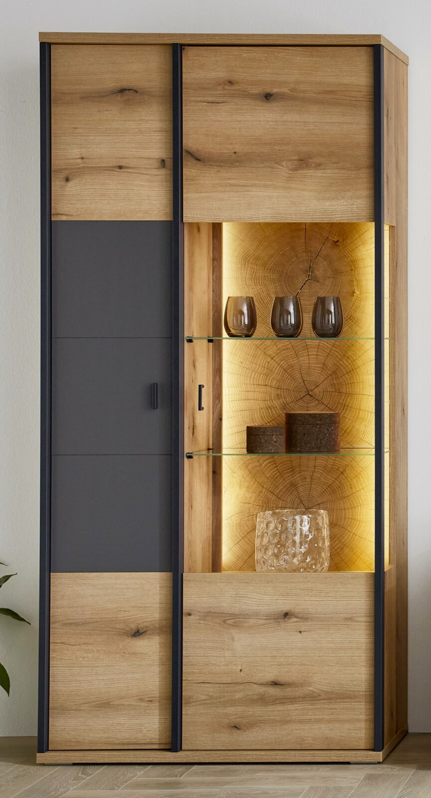 XORA Vitrine MELO Moderne vitrinekast van licht hout met een zwarte voorkant en een open, verlichte glazen plank; gefotografeerd vanaf de voorkant in een licht schuin perspectief vanaf de rechterkant.