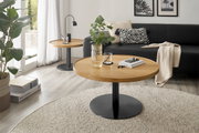 Moderne salontafel met een rond houten blad en een zwart metalen onderstel, in de woonkamer met een bank en planten, gezien van voren.