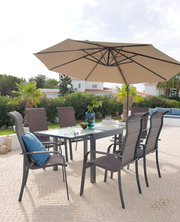 Großer, beiger Sonnenschirm über einem modernen Gartentisch mit sechs Stühlen, umgeben von grüner Vegetation und einem hellen Himmel. Perspektive von schräg unten.