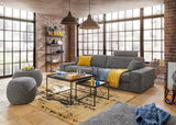 Großes, modernes Big-Sofa in einem stilvollen Wohnzimmer mit Backsteinwänden und großen Fenstern, seitliche Perspektive.