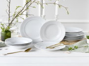 Weißes Porzellan-Tafelservice mit dezentem Reliefdekor (Speiseteller, Suppenteller und Schalen) auf hellem Holztisch, dekoriert mit goldfarbenem Besteck und Frühlingszweigen, frontal in leichter Schrägansicht aufgenommen.