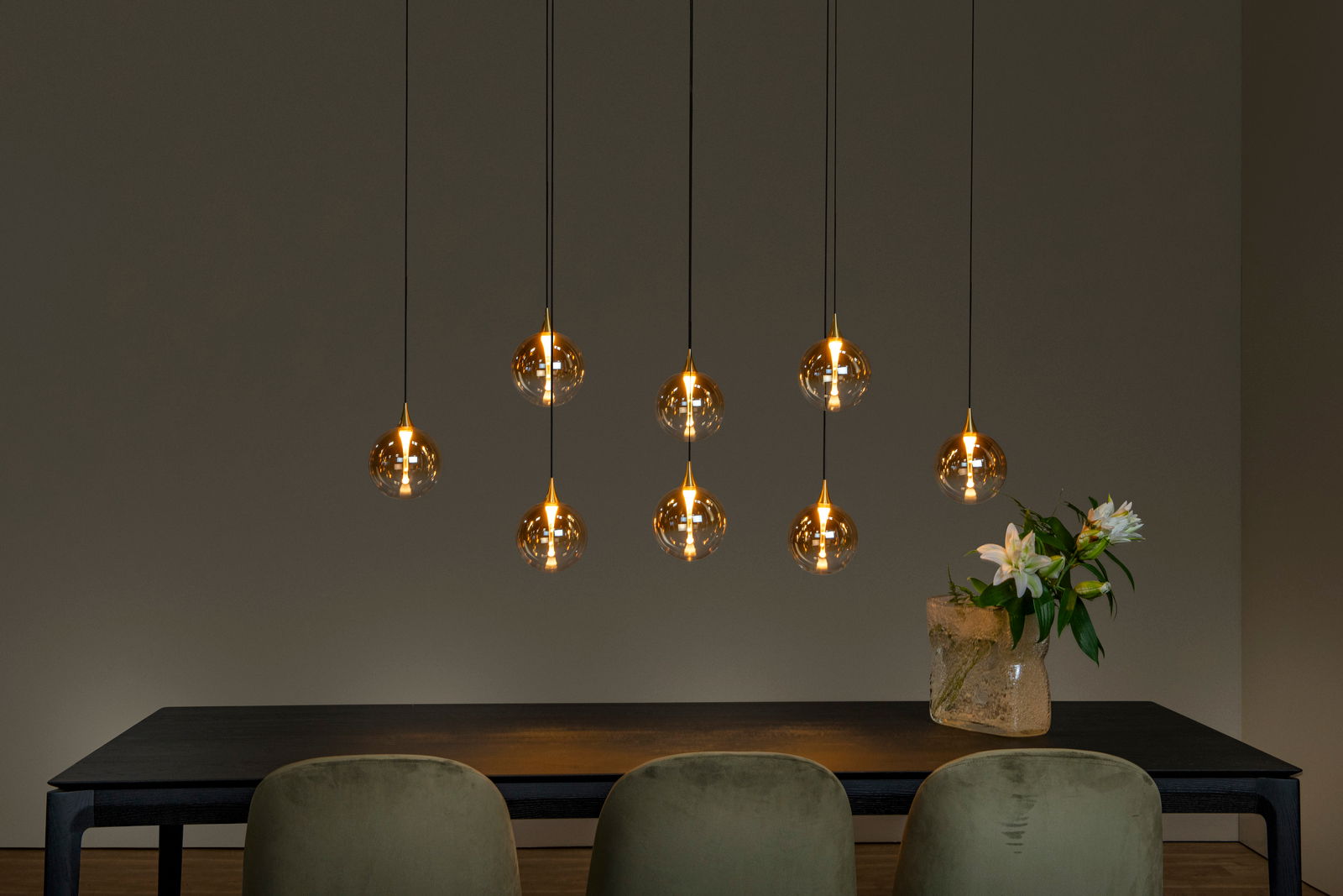 Moderne Hängeleuchte mit sieben kugelförmigen, goldenen Lampenschirmen über einem Esstisch, seitliche Perspektive.