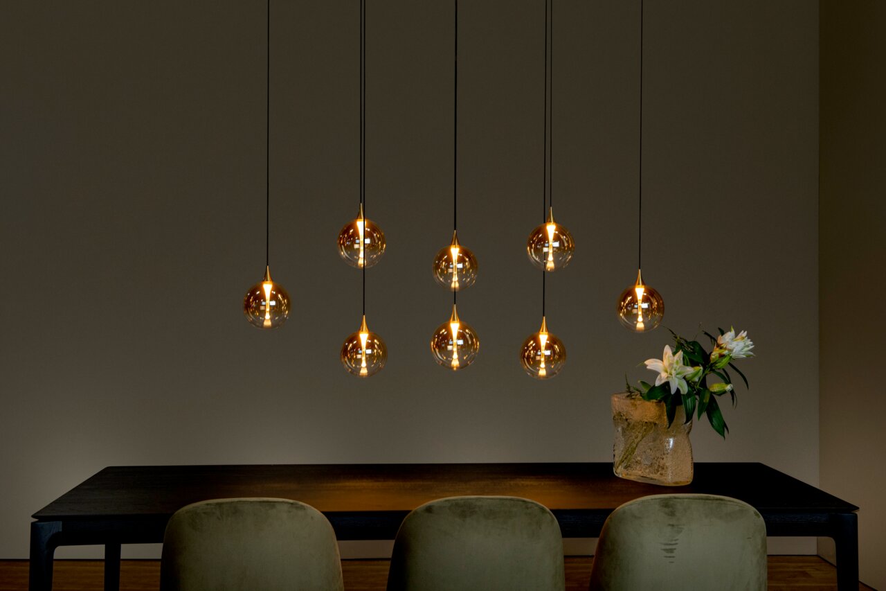 Moderne Hängeleuchte mit sieben kugelförmigen, goldenen Lampenschirmen über einem Esstisch, seitliche Perspektive.