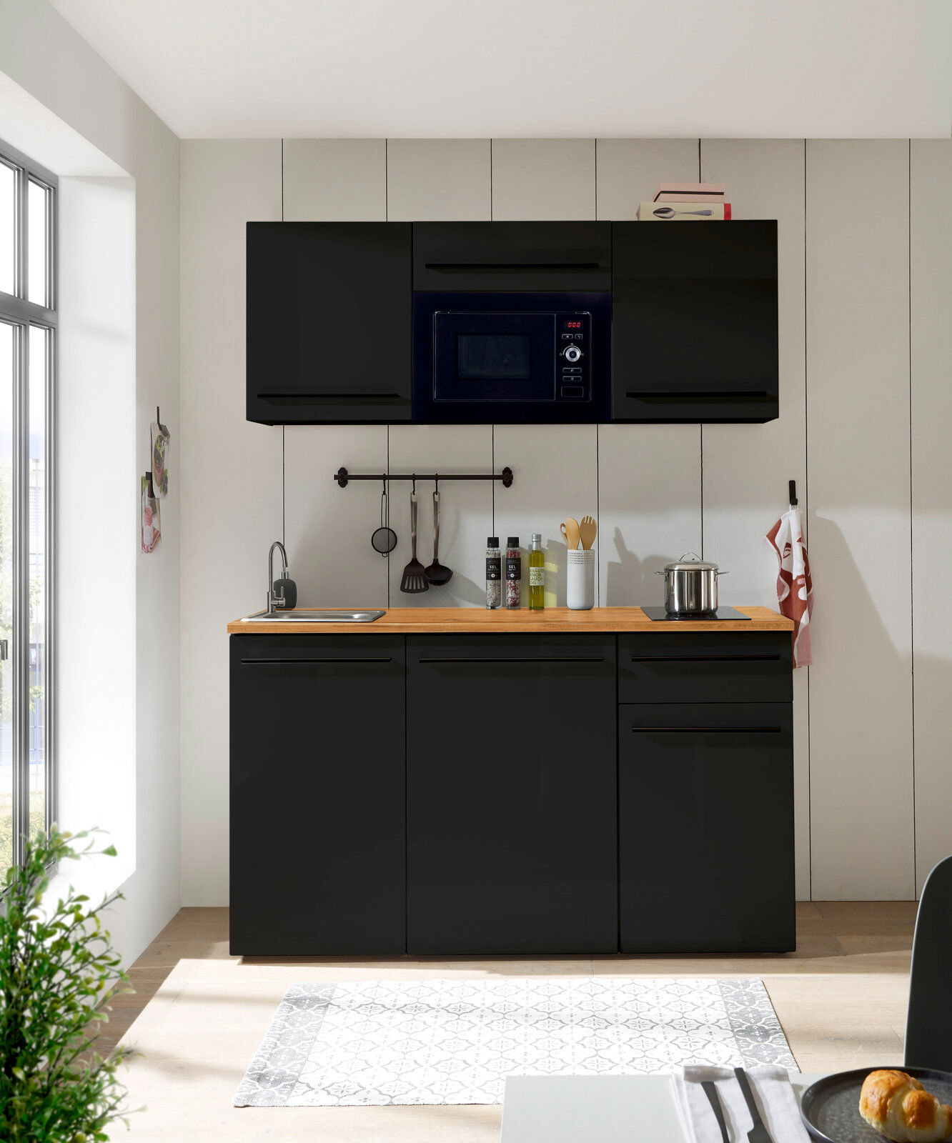 Moderne Single-Küche 160 in schwarzem Design mit Hängeschränken, Mikrowelle, Spüle und Kochfeld, frontal betrachtet.