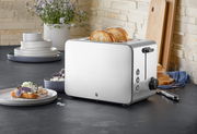 Silberner WMF Stelio Toaster Edition mit zwei Scheiben Toast, seitliche Perspektive, auf einer Küchenarbeitsplatte mit Geschirr im Hintergrund.