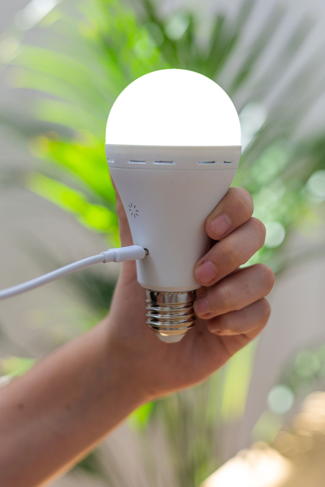 Eine Hand hält ein leuchtendes Akku-Leuchtmittel, das über ein Kabel aufgeladen wird. Perspektive von der Seite.