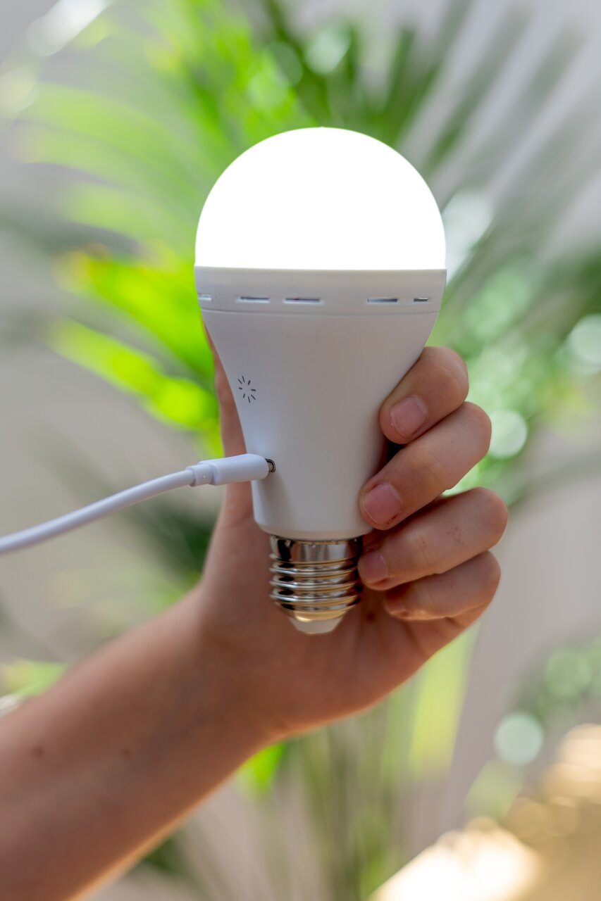 Een hand houdt een oplichtende oplaadbare lamp vast, die via een kabel wordt opgeladen. Zijaanzicht.