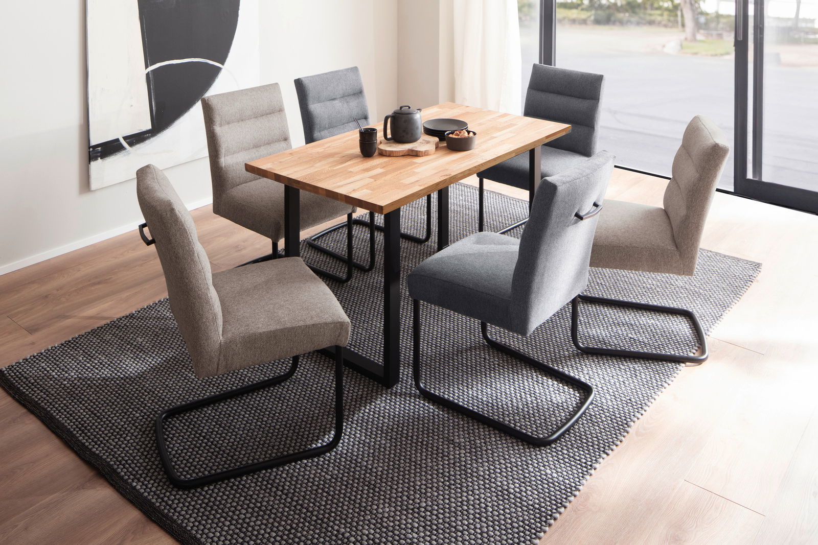 Moderner Esstisch mit Holzplatte und schwarzen Metallbeinen, umgeben von sechs gepolsterten Stühlen in Grau- und Beigetönen, aus der Vogelperspektive fotografiert.