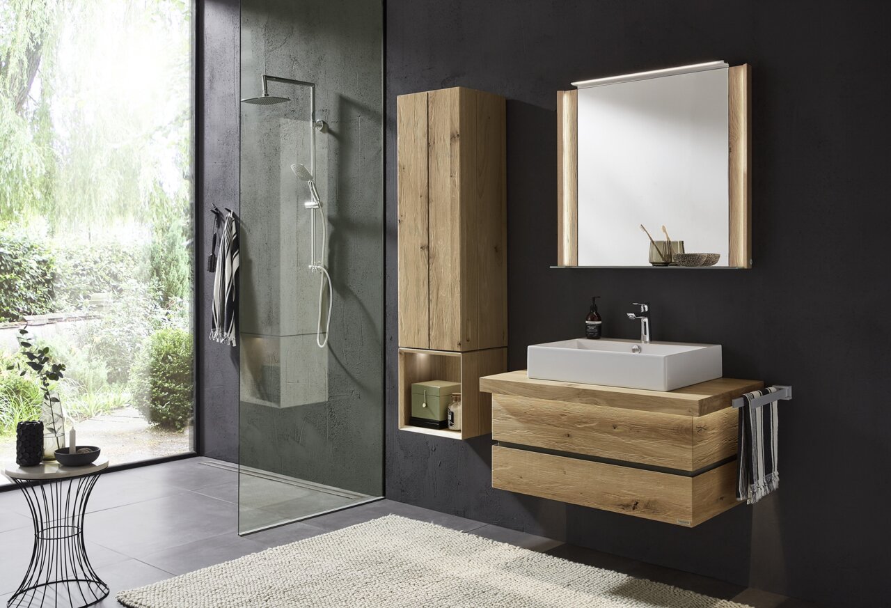 Valdera Badkombination FRESH Moderne Badkombination mit Holzoptik, bestehend aus einem Waschtisch mit integriertem Waschbecken, einem hohen Schrank und einem beleuchteten Spiegel, seitliche Perspektive.
