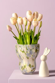 Vase mit buntem Muster und Tulpen, neben einer kleinen Hasenfigur, aus seitlicher Perspektive fotografiert.