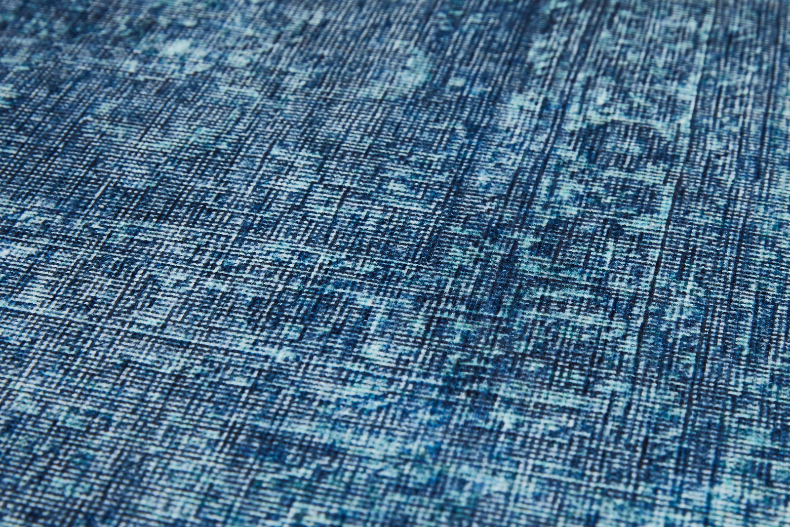 Nahaufnahme eines blauen Teppichs mit abstraktem Muster, schräg von der Seite fotografiert.