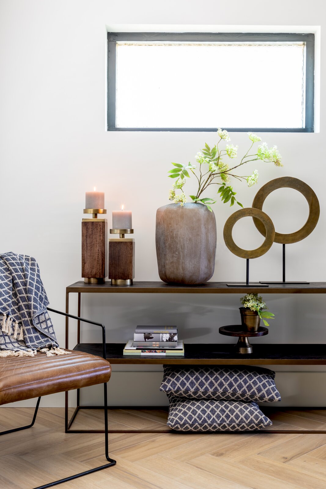 Woonkamerdecoratie met moderne kandelaars, een grote vaas met groene takken en een decoratieve metalen ring op een plank. Aanzicht van voren.