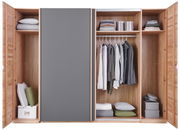 Offener Schwebetürenschrank aus Holz mit grauer Tür, gefüllt mit Kleidung, Kissen und Aufbewahrungsboxen, frontale Ansicht.