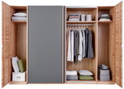 Offener Schwebetürenschrank aus Holz mit grauer Tür, gefüllt mit Kleidung, Kissen und Aufbewahrungsboxen, frontale Ansicht.