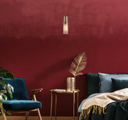 Moderne Hängeleuchte in einem stilvollen Wohnzimmer mit roter Wand, blauer Samtsessel und goldenen Akzenten, seitliche Perspektive.