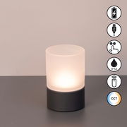 Akku-Windlicht mit zylindrischem, mattem Glas und dunklem Sockel, frontal fotografiert. Symbole für USB-Ladung, Touch-Bedienung, IP54-Schutz, Fernbedienung und CCT-Farbtemperaturwechsel sind sichtbar.