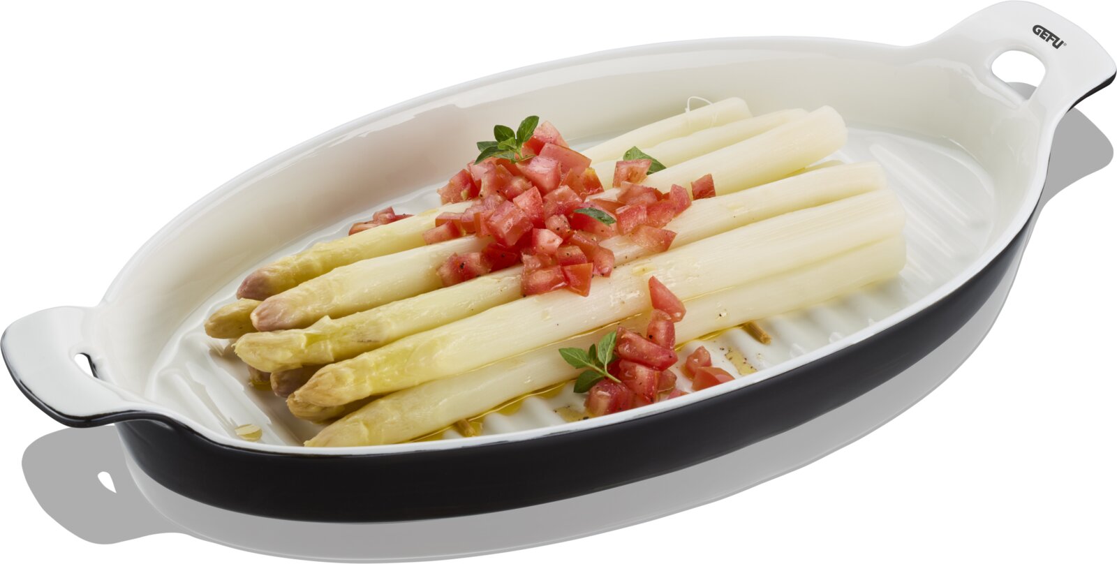 Weiße ovale Auflaufform mit seitlichen Griffen, gefüllt mit weißem Spargel und Tomatenwürfeln als Topping, in schräger Draufsicht vor weißem Hintergrund.