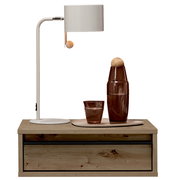 Weiße Tischlampe mit zylindrischem Schirm und Holz-Zugknopf auf einem Holz-Nachttisch, daneben braune Glasflasche und Glas auf Tablett, frontal aus leicht erhöhter Perspektive.