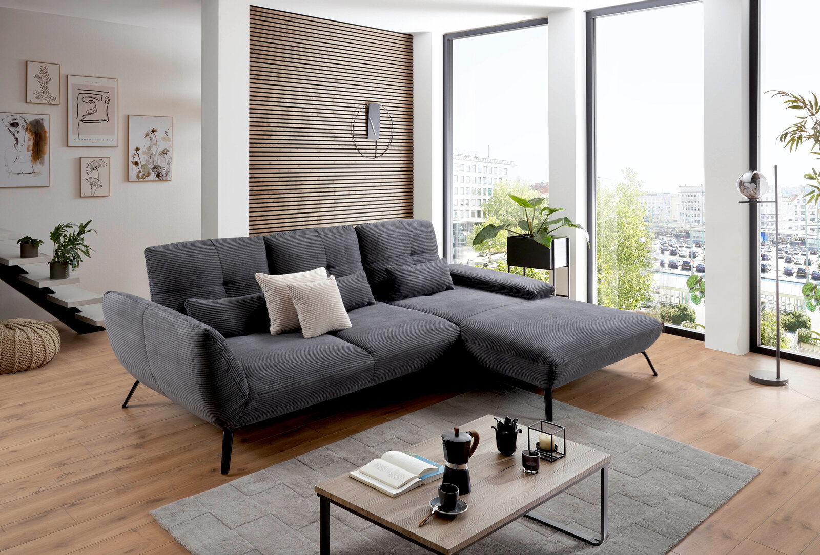 Graues Ecksofa in modernem Wohnzimmer mit großen Fenstern, von vorne betrachtet.