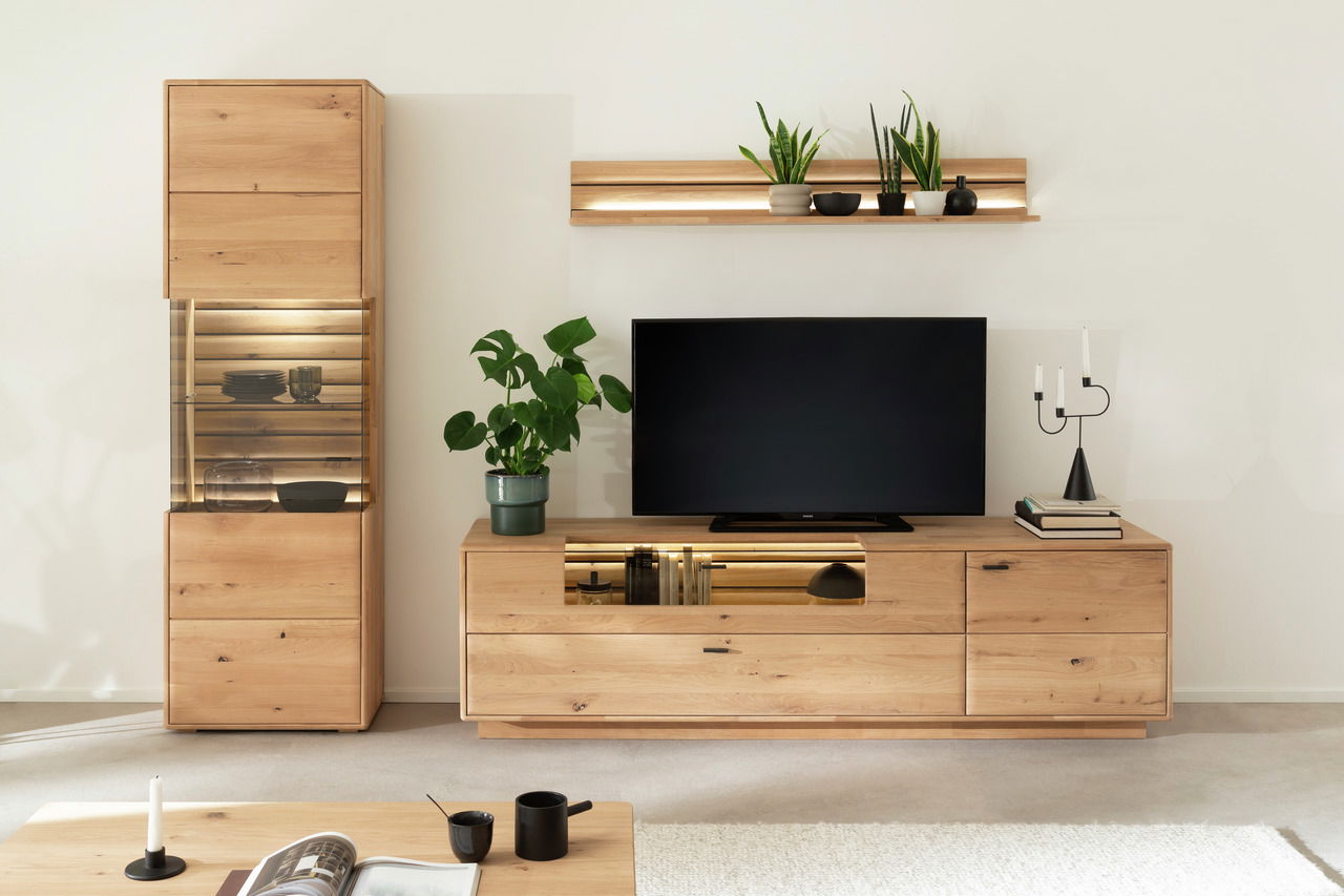 Linea Natura Wandkombination GEORGIA Moderne Wandkombination aus Holz mit TV-Schrank, Vitrine und Regal, dekoriert mit Pflanzen und Kerzen, aus frontaler Perspektive.