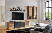 Moderne Wohnzimmer-Wohnwand in Eiche-Optik mit schwarzen Fronten, Lowboard, Wandregal und zwei Hängeschränken neben einem wandmontierten TV, fotografiert in frontaler leicht seitlicher Perspektive.