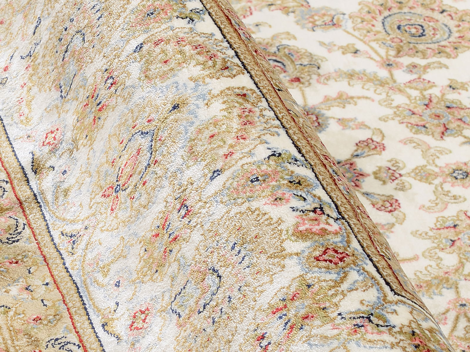 Nahaufnahme eines Orientteppichs mit floralen Mustern in Beige, Rot und Blau, leicht aufgerollt.