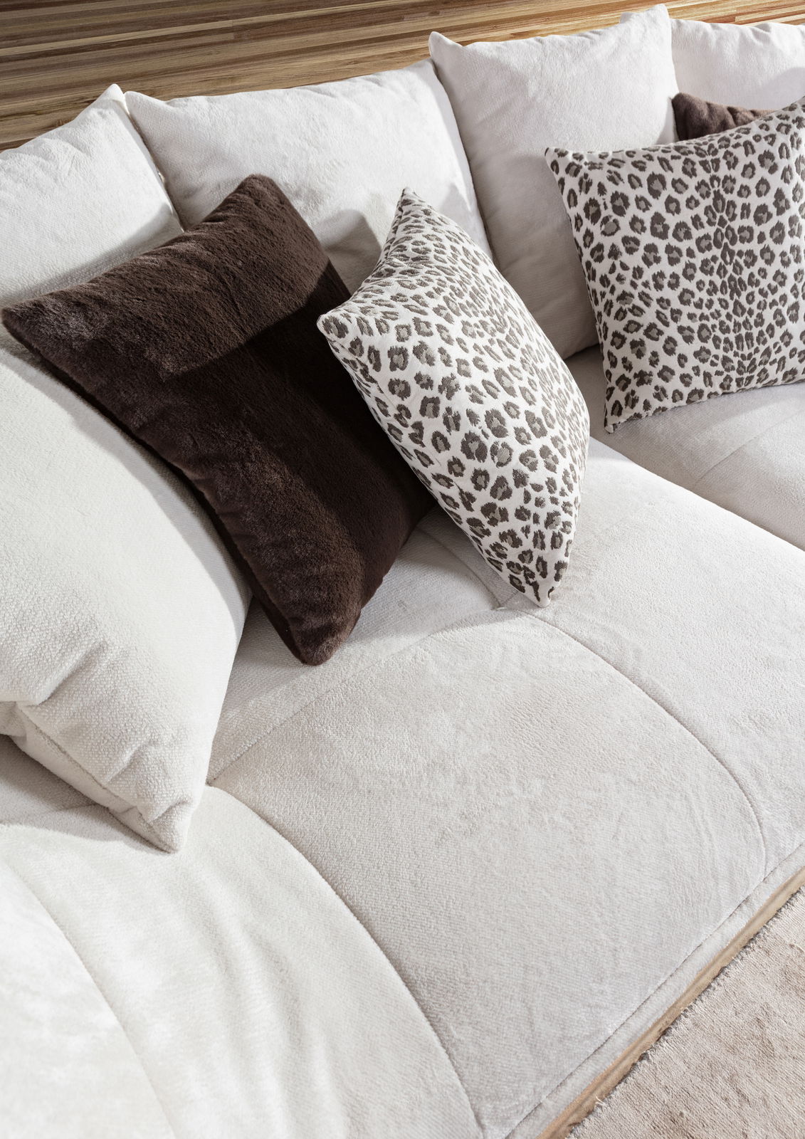 Nahaufnahme eines Megasofas mit weichen, cremefarbenen Kissen und dekorativen Kissen mit Leopardenmuster, seitliche Perspektive.