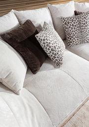 Nahaufnahme eines Megasofas mit weichen, cremefarbenen Kissen und dekorativen Kissen mit Leopardenmuster, seitliche Perspektive.