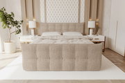Beiges, gepolstertes Polsterbett mit gestepptem Kopf- und Fußteil in modernem Schlafzimmer, frontale Perspektive von vorn.