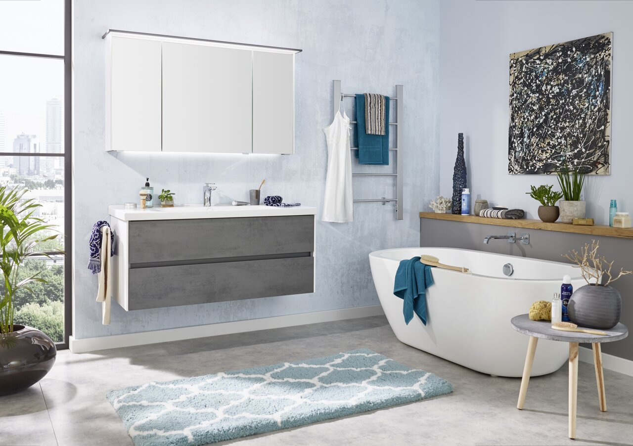 Moderne Badezimmerkombination mit grauem Waschtisch, großem Spiegel und freistehender Badewanne, seitliche Perspektive