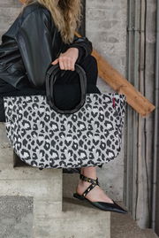 Große Tasche mit Leopardenmuster, gehalten von einer Person in schwarzer Kleidung, seitliche Perspektive.