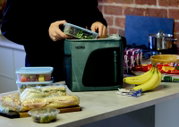 Thermos Kühltasche in Grün und Schwarz aus frontaler Perspektive, während sie in einer Küche mit einer Salatdose und weiteren Speisen befüllt wird