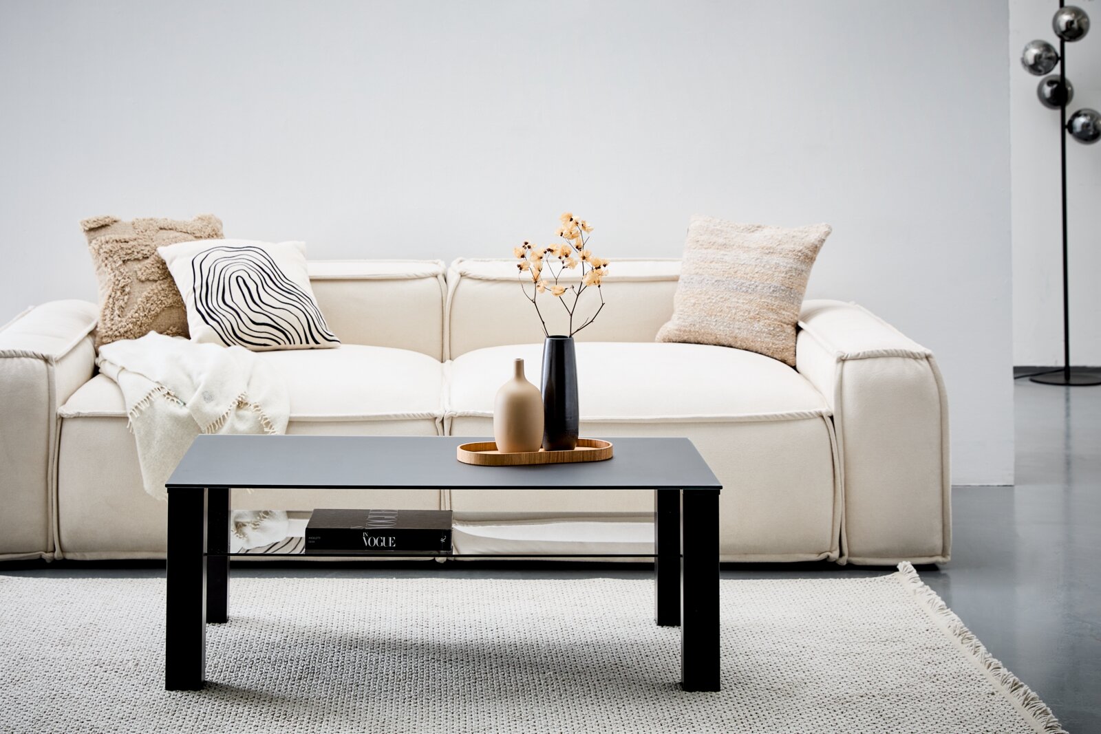 XORA Salontafel ROMINA Moderner Couchtisch XORA Tisch ROMINA in schwarzem Design, frontal vor einem cremefarbenen Sofa mit dekorativen Kissen und Vasen auf dem Tisch.