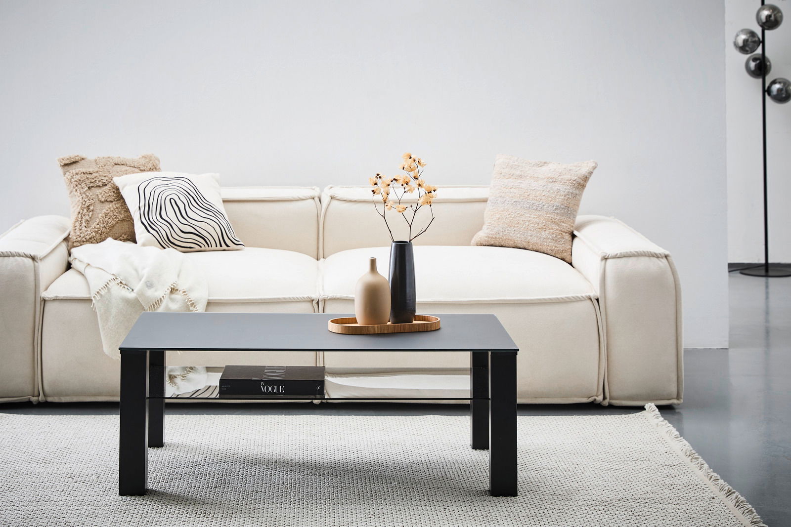 Moderner Couchtisch XORA Tisch ROMINA in schwarzem Design, frontal vor einem cremefarbenen Sofa mit dekorativen Kissen und Vasen auf dem Tisch.