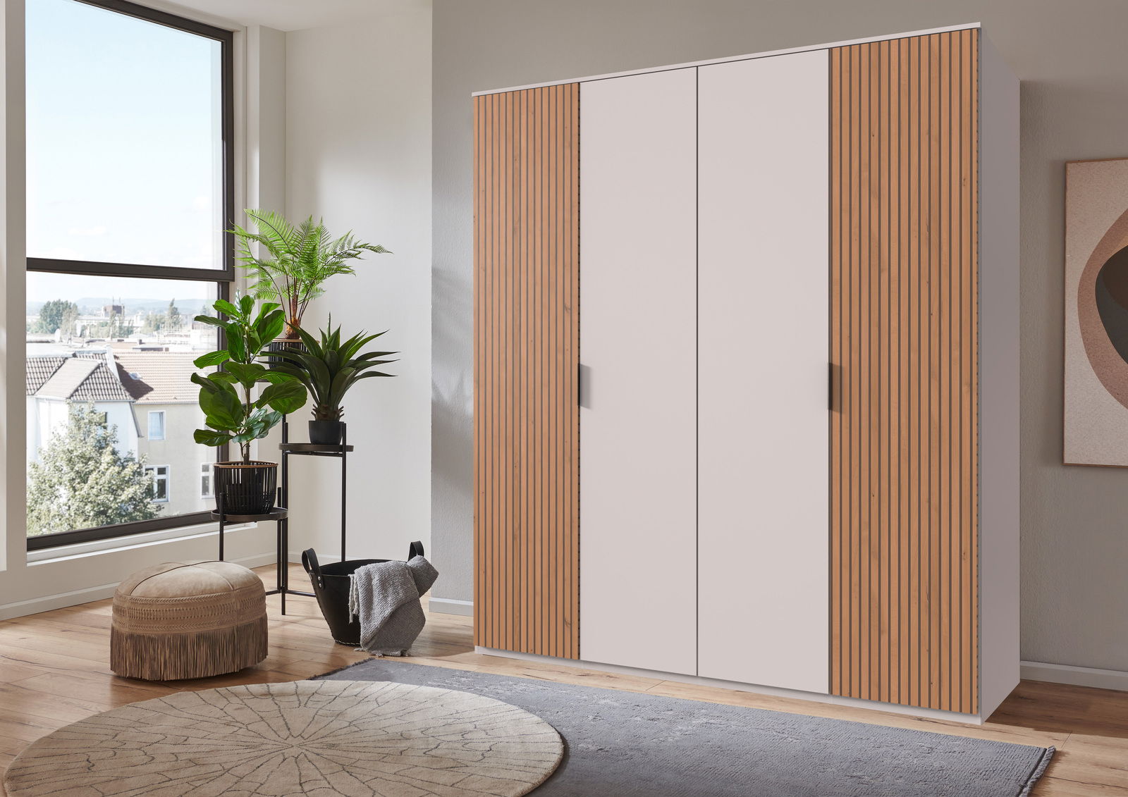 Moderner Drehtürenschrank mit vier Türen, teilweise mit Holzlamellen, in einem hellen Raum mit Pflanzen und großen Fenstern, seitliche Perspektive.