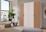 Moderner Drehtürenschrank mit vier Türen, teilweise mit Holzlamellen, in einem hellen Raum mit Pflanzen und großen Fenstern, seitliche Perspektive.