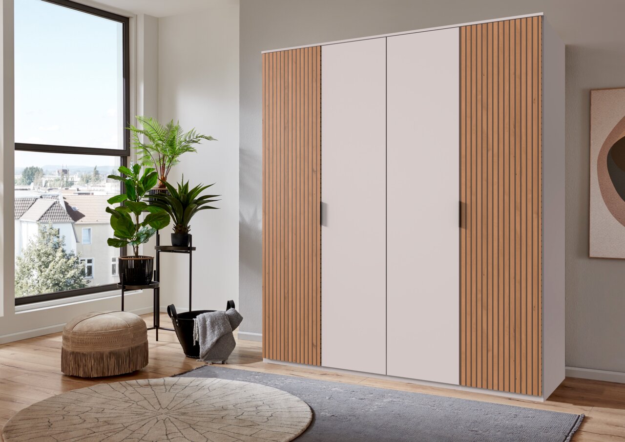 Moderne kast met vier draaideuren, deels met houten lamellen, in een lichte ruimte met planten en grote ramen, zijaanzicht.